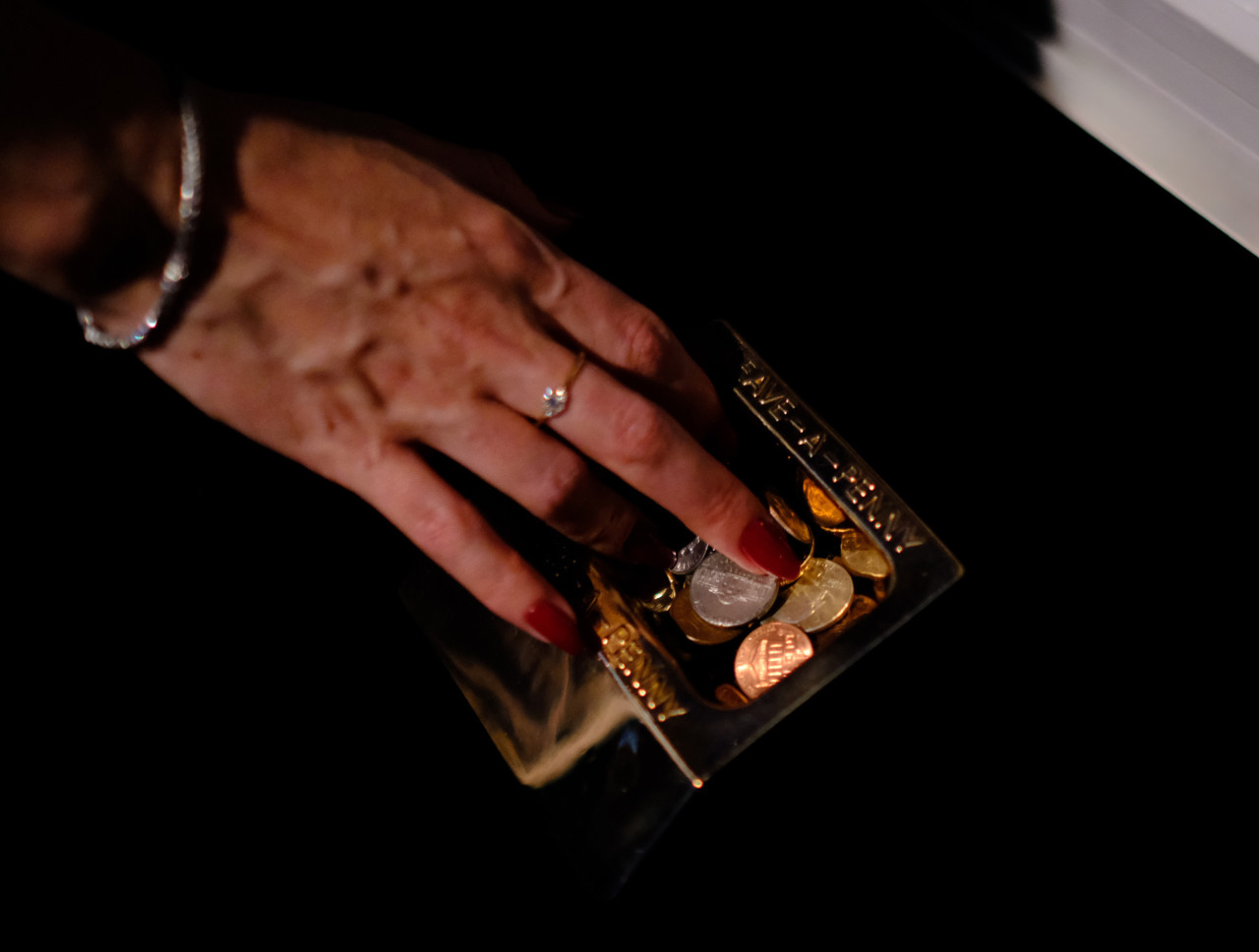 A hand reaches into a bronze penny-share dish filled with coins.