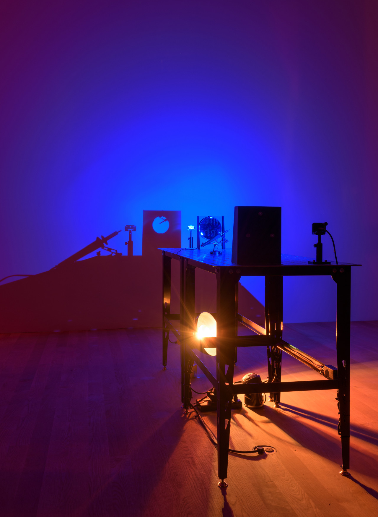 In a darkened room, a bright blue LED light, two circular mirrors and scientific mounts sit atop two metal welding tables.