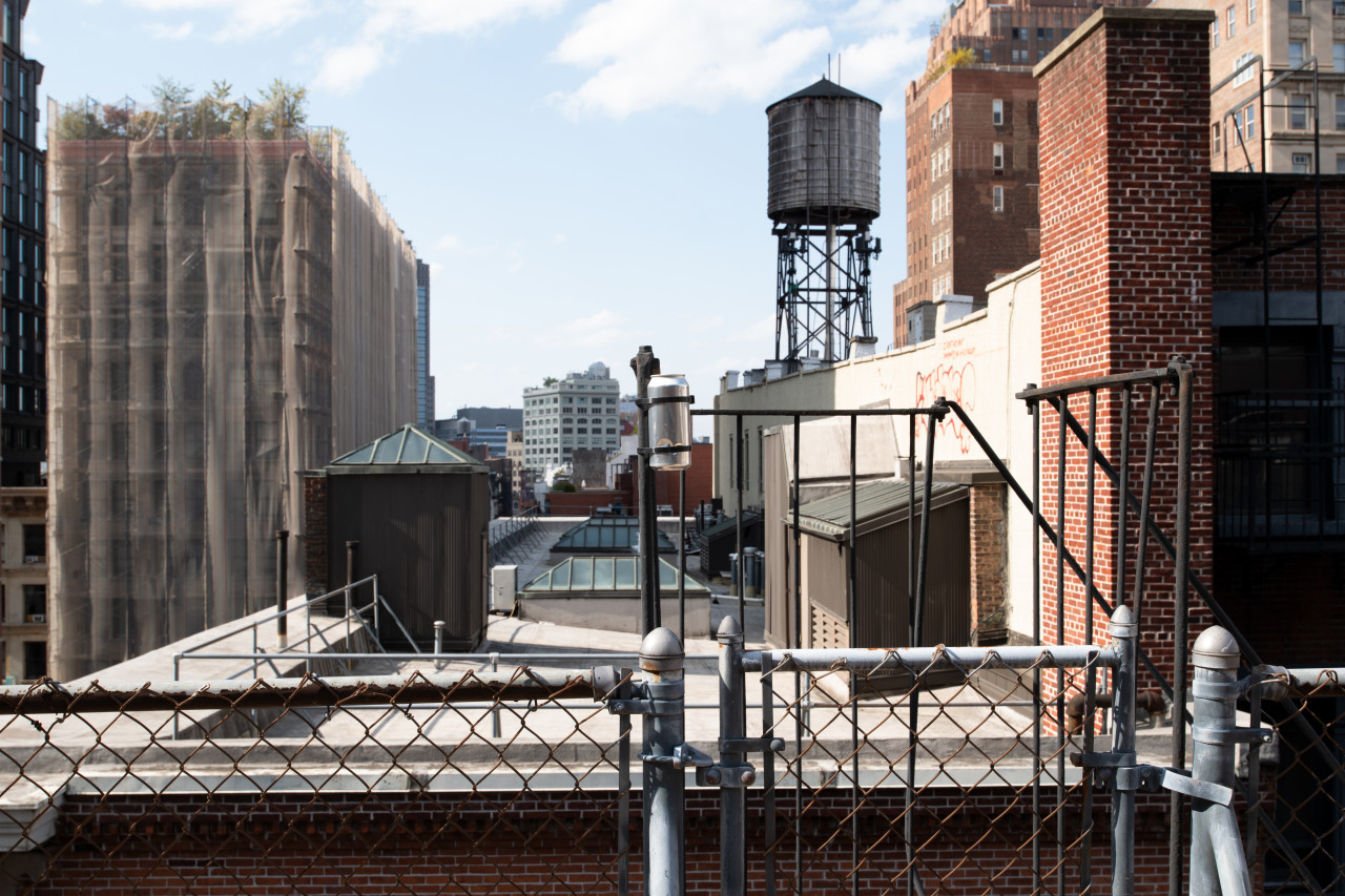 Against an urban landscape, a metal pinhole camera tin is mounted to a roof post.
