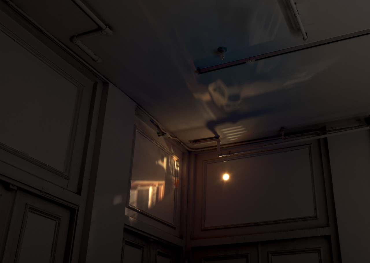 In the corner of a darkened room, a blacked out window hosts a small lens, which projects an image of the crosswalk outside the building onto the wall and ceiling inside.