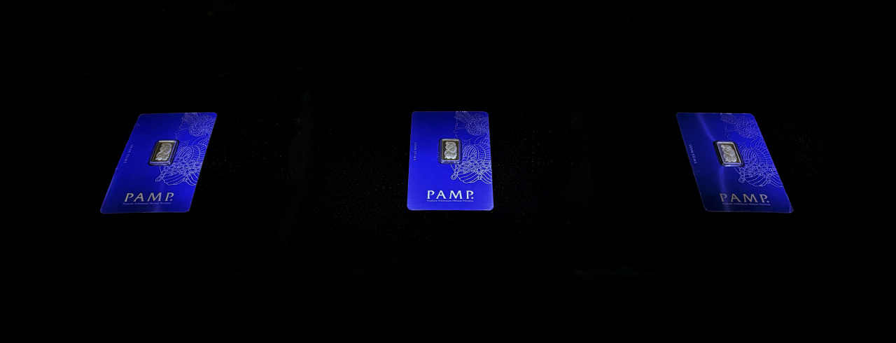 A takeaway artwork shows three 2.5 gram gold bullion bars in blue Pamp Suisse certifying cases. Each bar depicts a low relief icon of Lady Fortuna, the blindfolded goddess of luck, fortune, and chance.