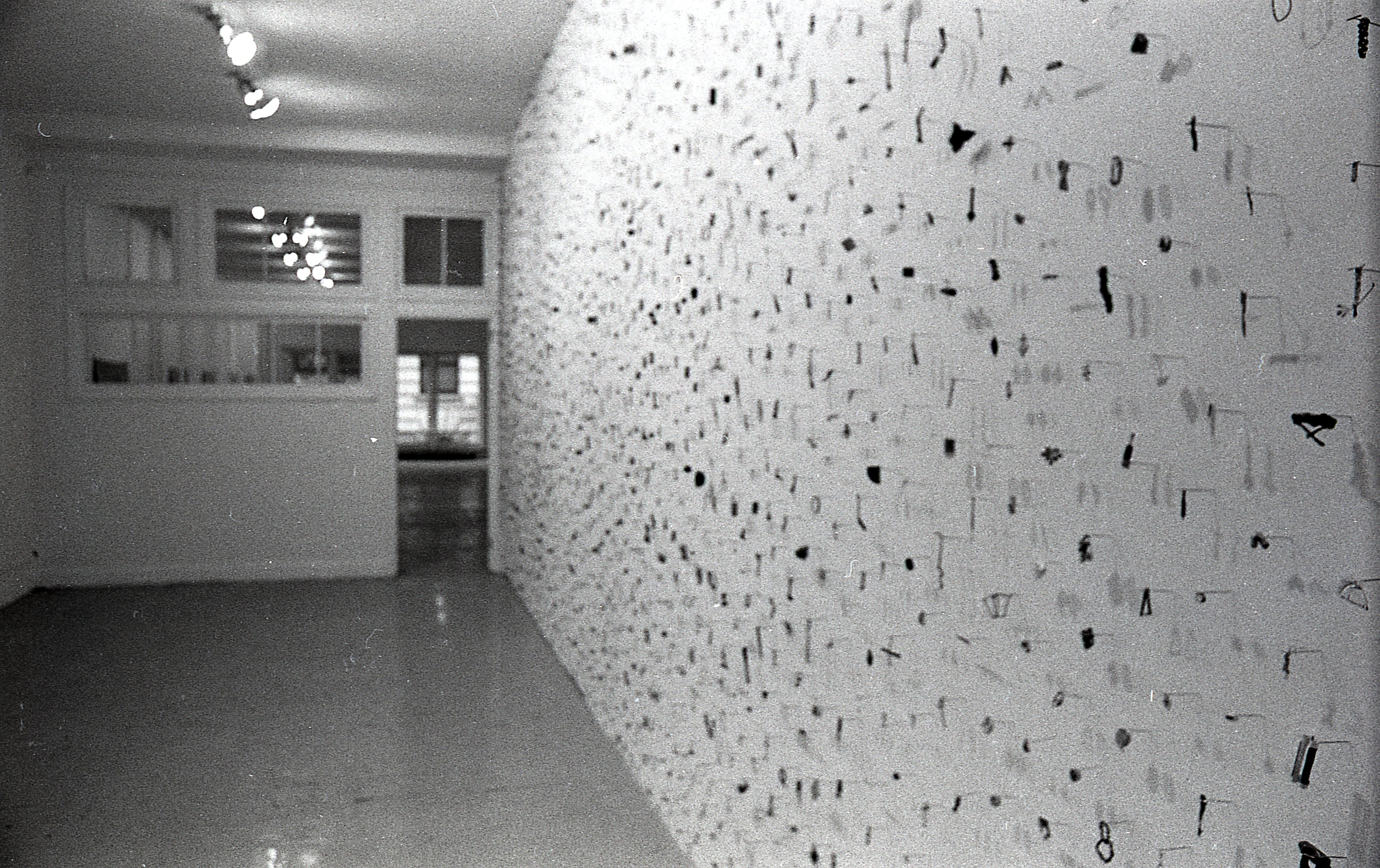 A photograph of small metal circles, bars, and other pieces mounted on a white gallery wall.