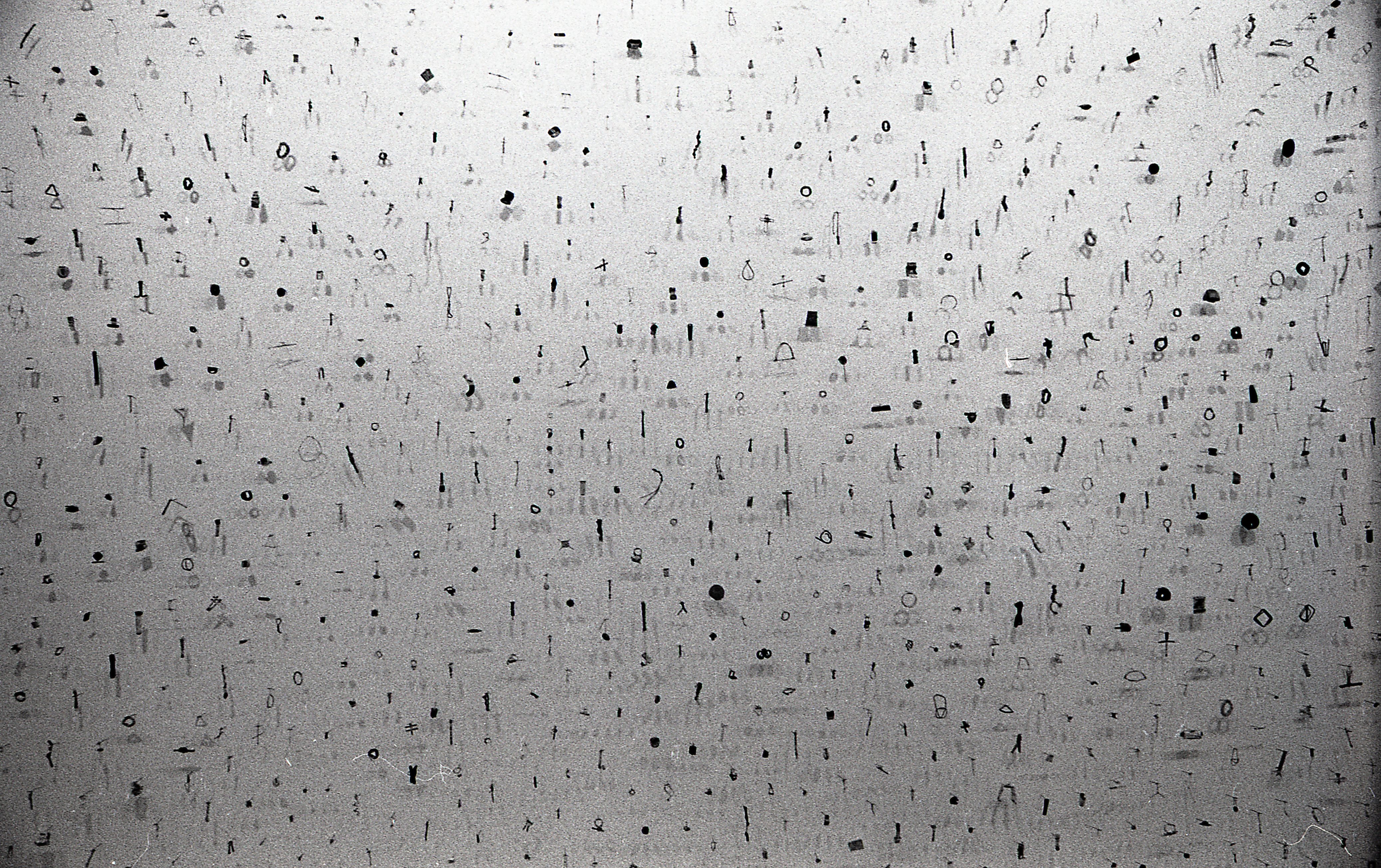 A photograph of small metal circles, bars, and other pieces mounted on a white gallery wall.