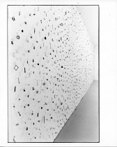 A photograph of small metal circles, bars, and other pieces mounted on a white gallery wall.