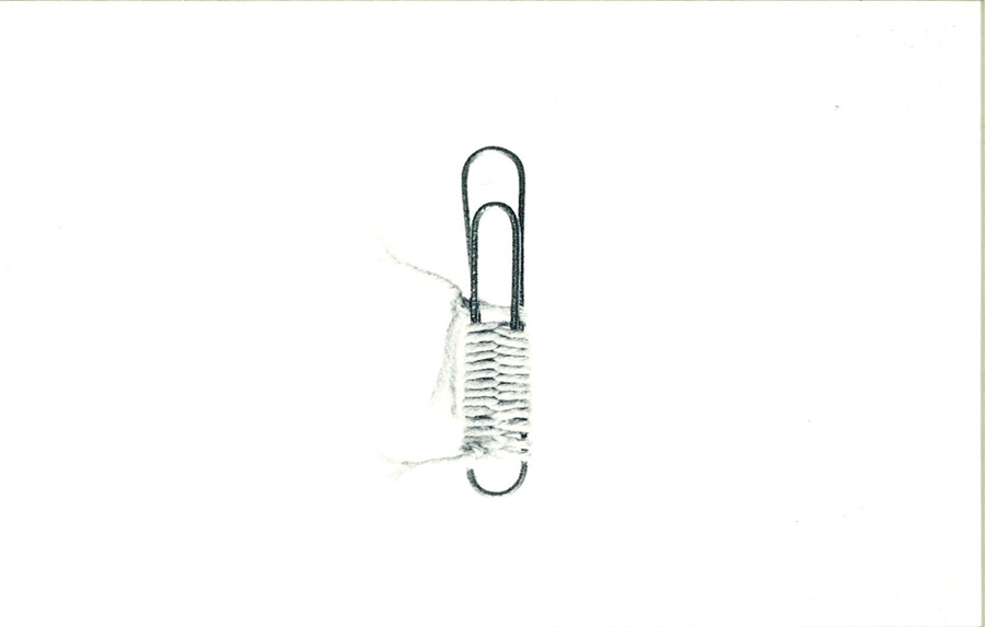 A paper clip is half-wrapped in twine on a white background.