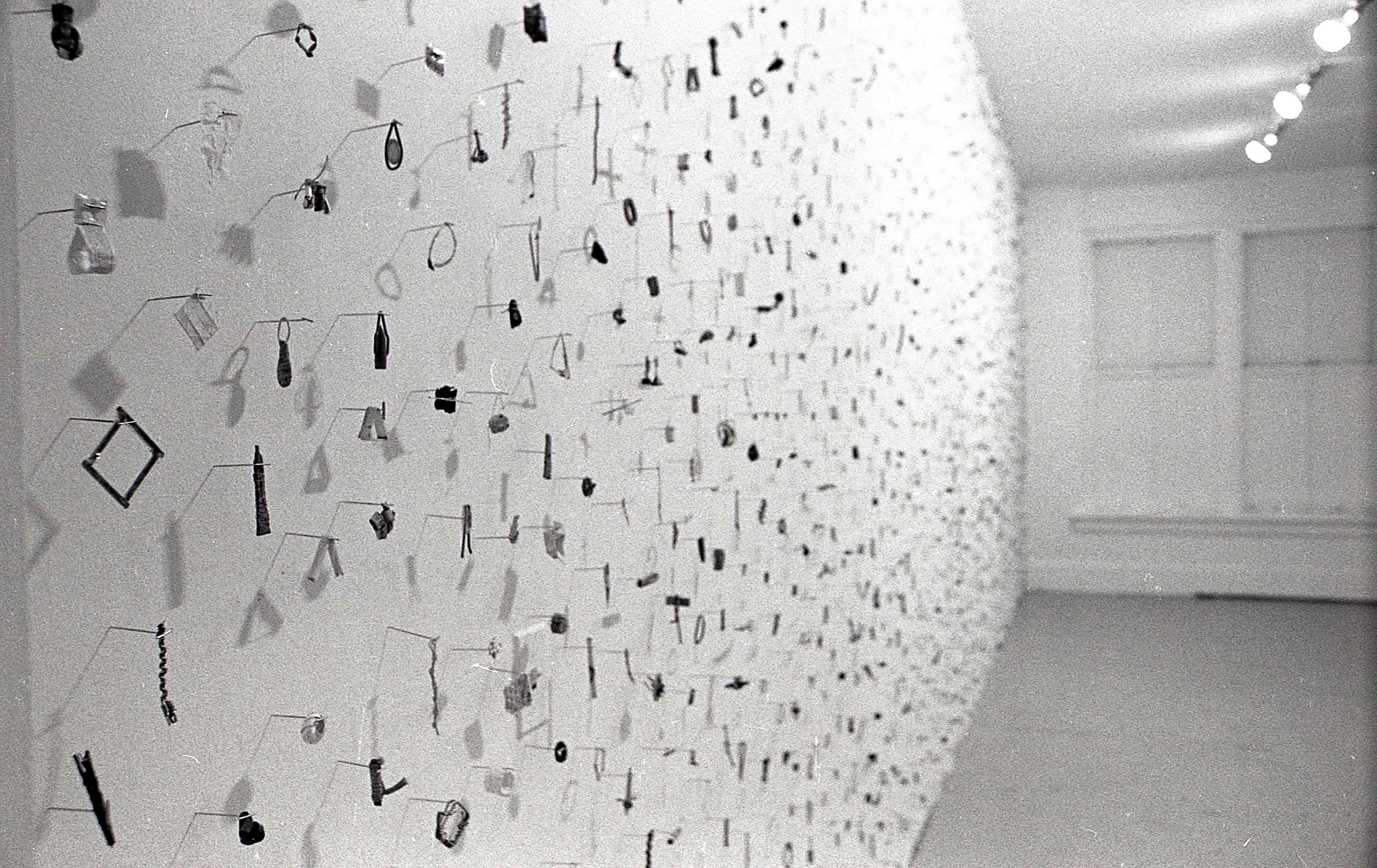 A photograph of small metal circles, bars, and other pieces mounted on a white gallery wall.