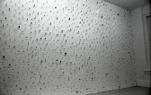 A photograph of small metal circles, bars, and other pieces mounted on a white gallery wall.