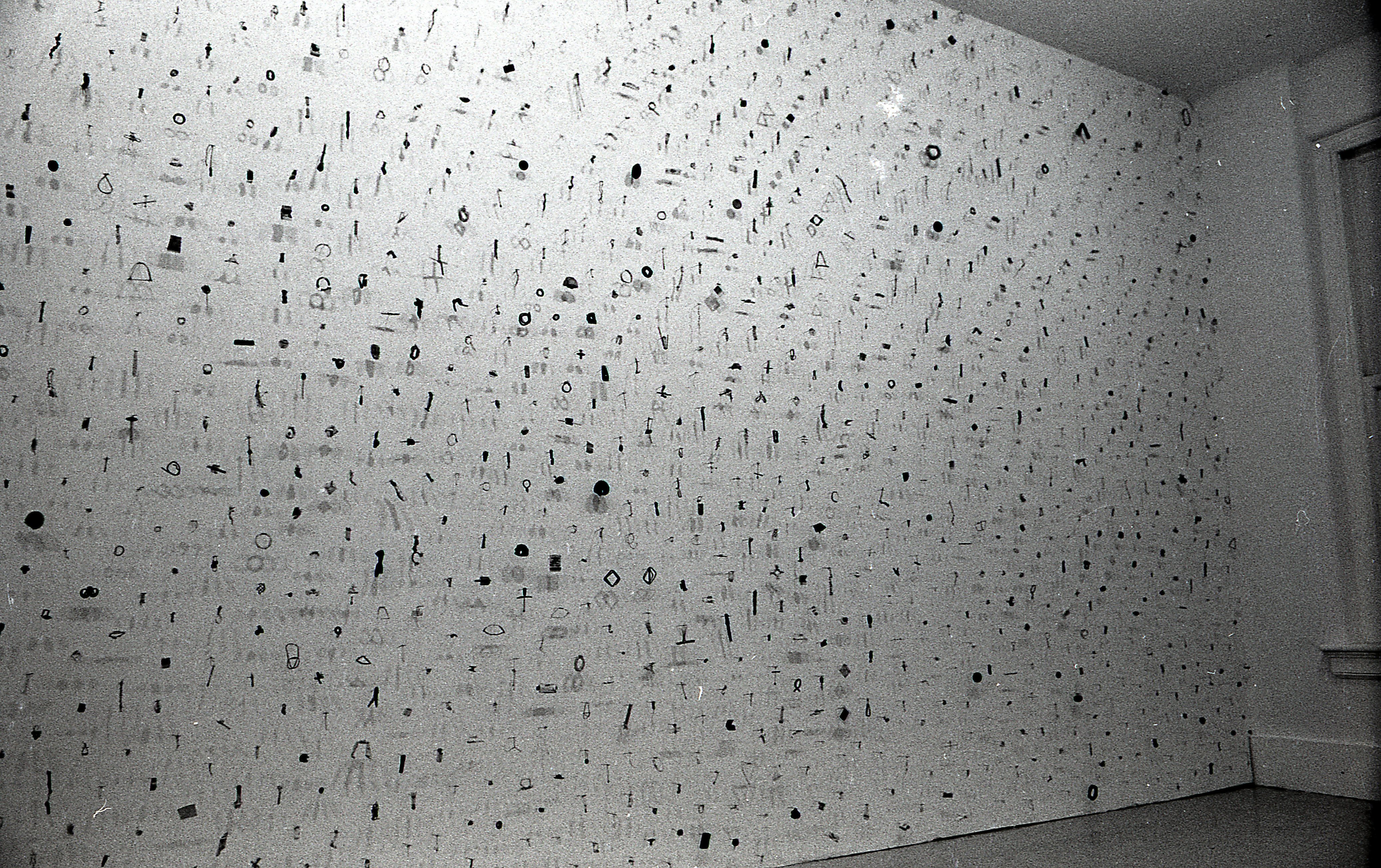 A photograph of small metal circles, bars, and other pieces mounted on a white gallery wall.