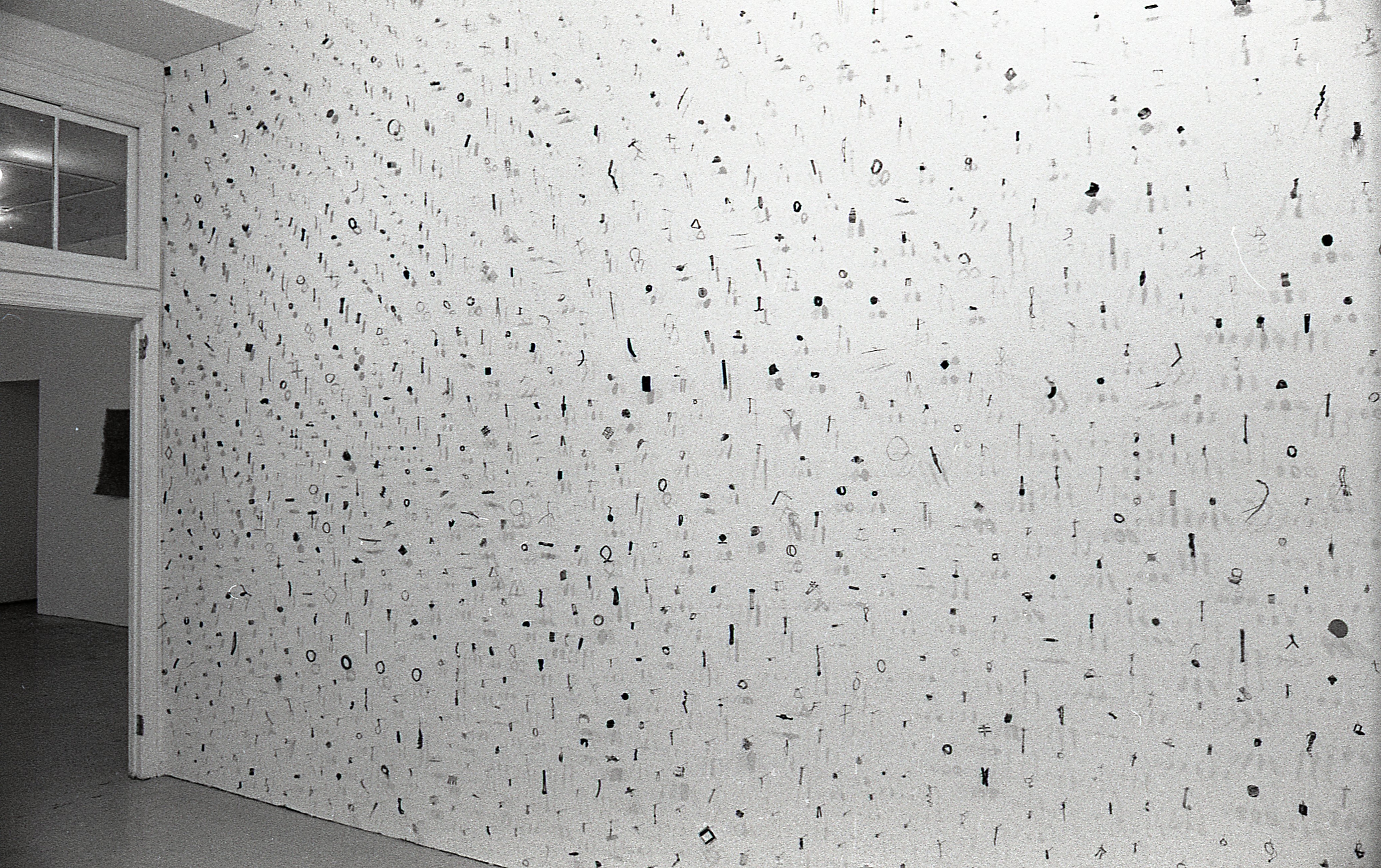 A photograph of small metal circles, bars, and other pieces mounted on a white gallery wall.