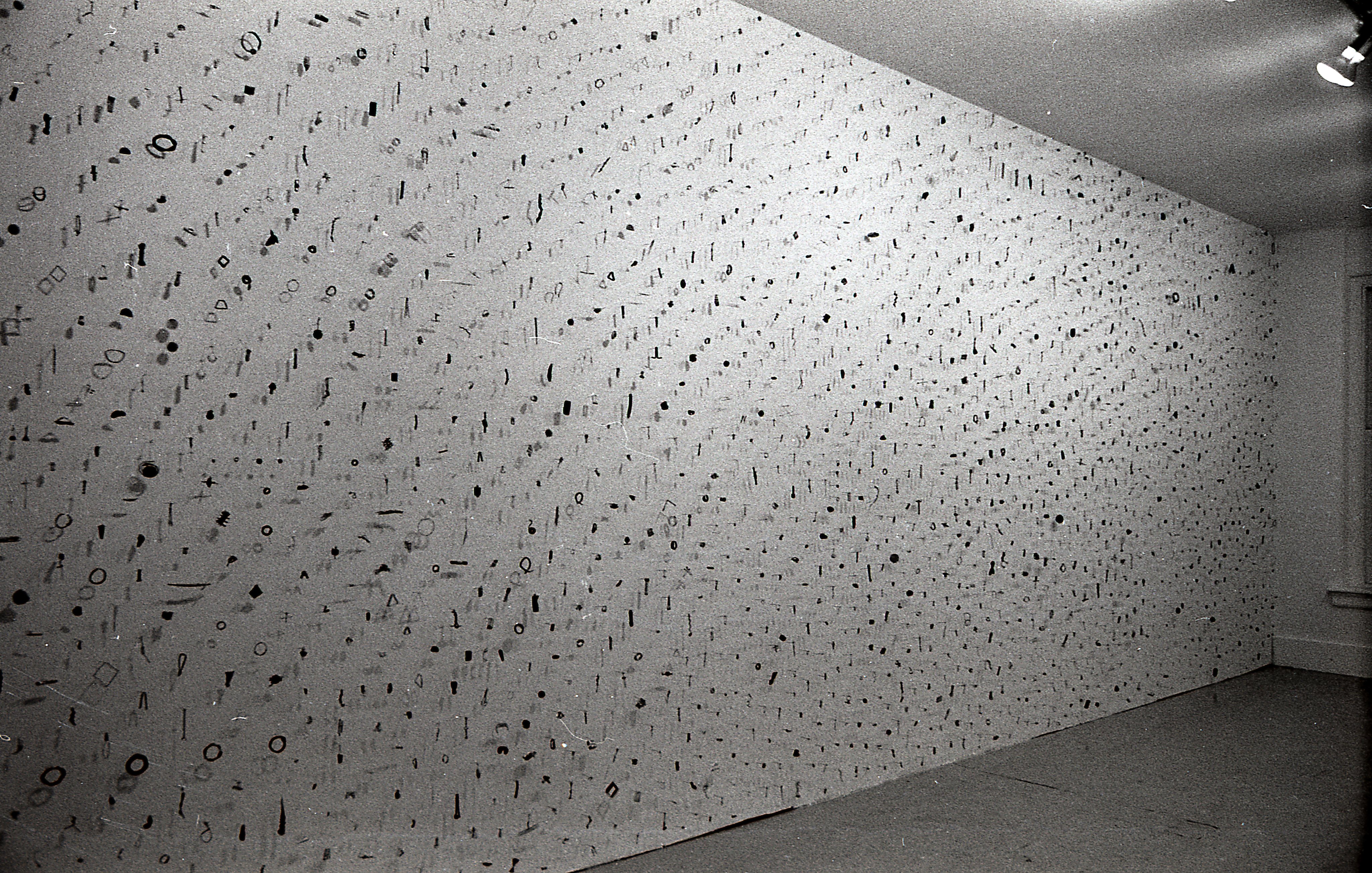 A photograph of small metal circles, bars, and other pieces mounted on a white gallery wall.