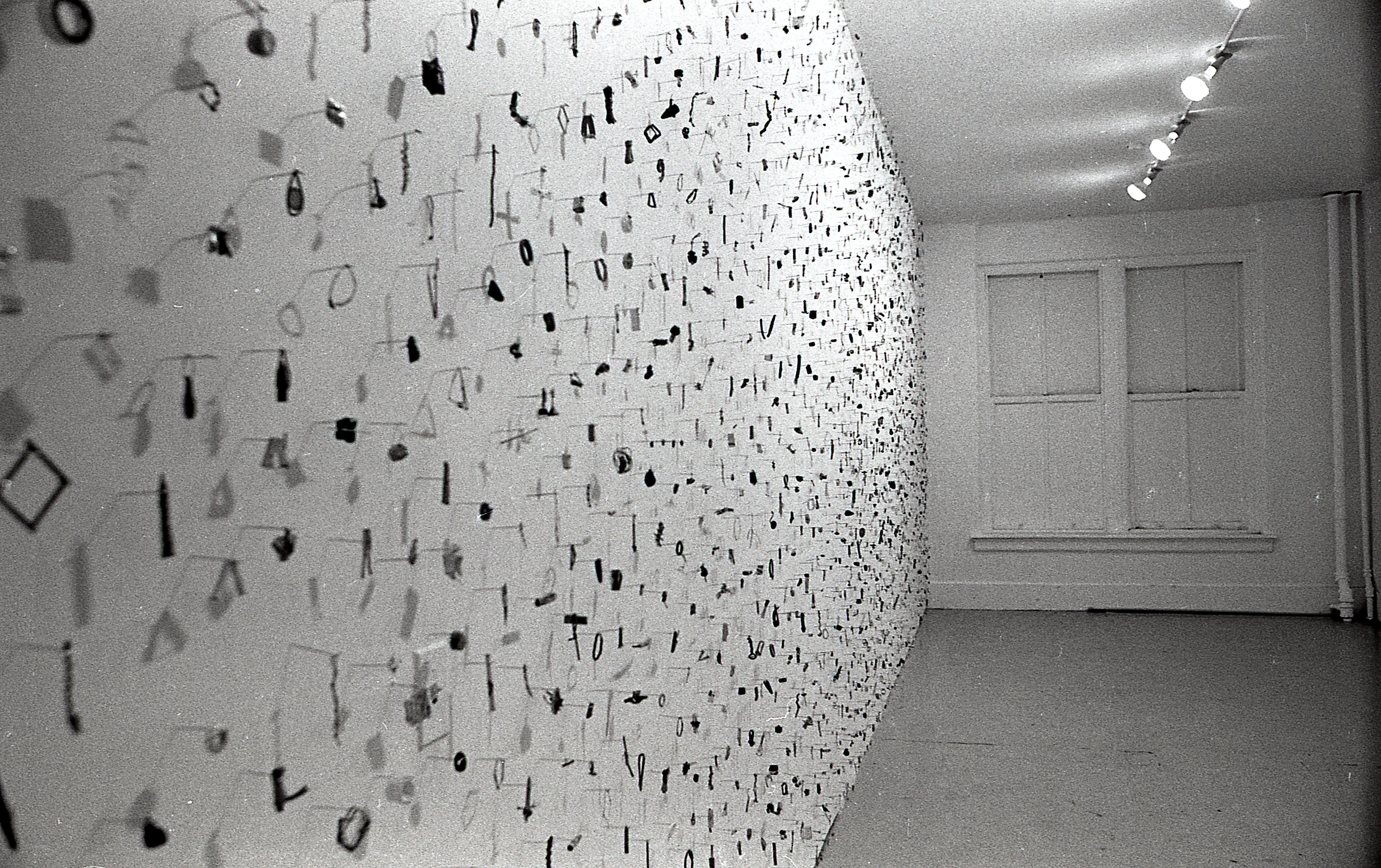 A photograph of small metal circles, bars, and other pieces mounted on a white gallery wall.
