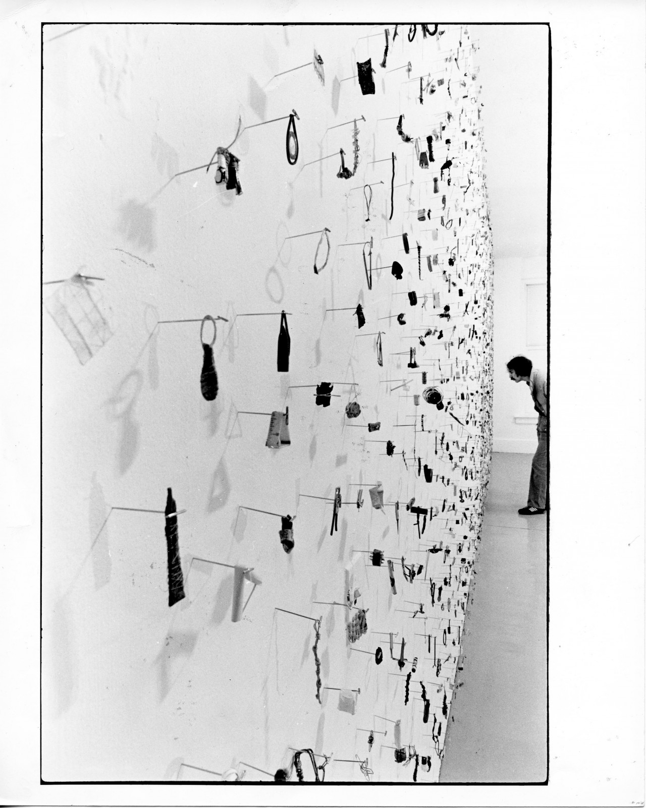 A photograph of small metal circles, bars, and other pieces mounted on a white gallery wall.