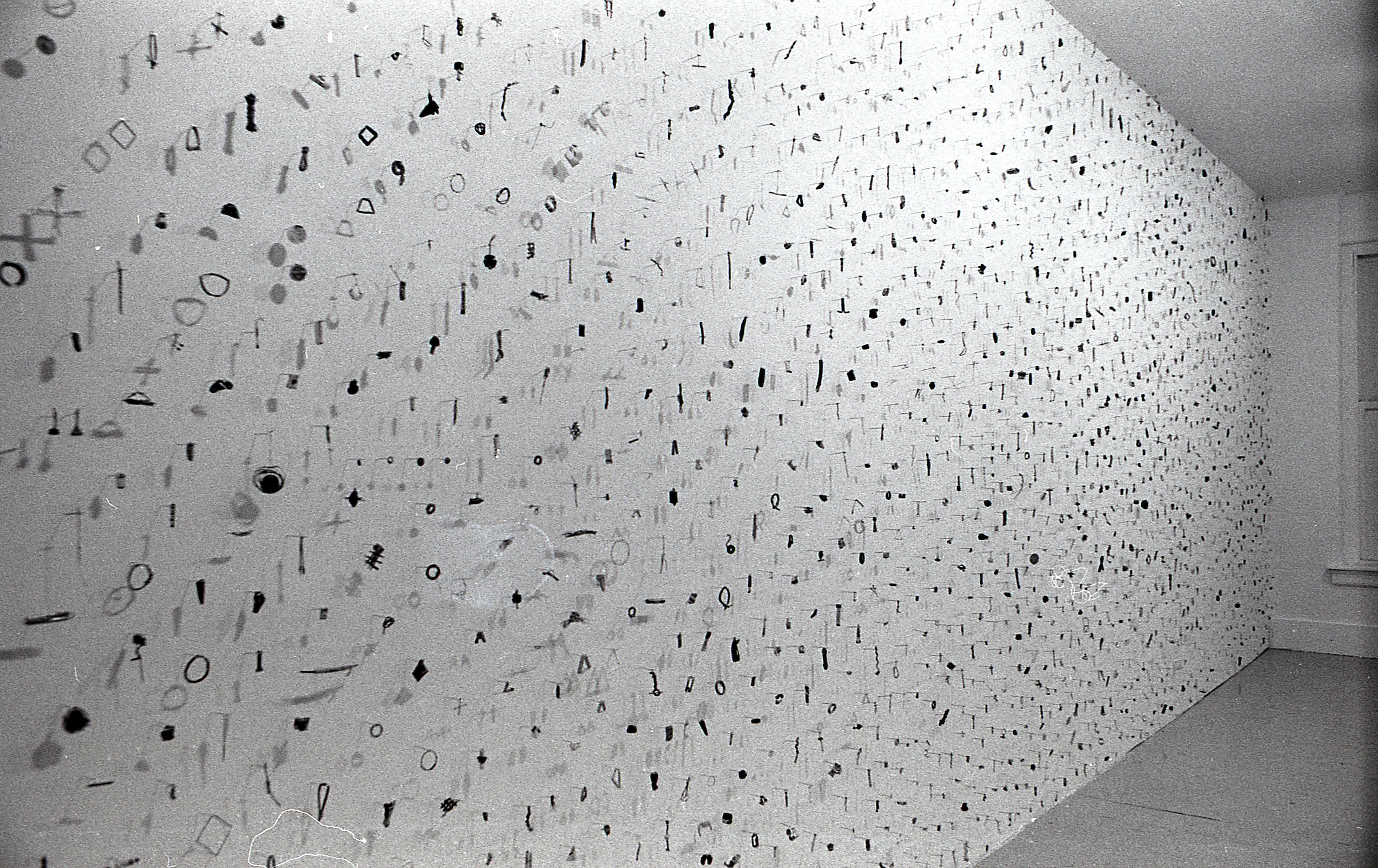 A photograph of small metal circles, bars, and other pieces mounted on a white gallery wall.