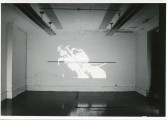 An image is projected onto a white wall. In the image, a figure plays a cello.
