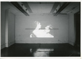 An image is projected onto a white wall. In the image, a woman holds a man's head in her hands.