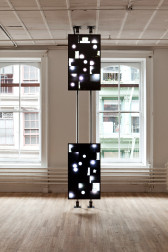 Two screens are mounted vertically on metal poles that stretch floor to ceiling. The screens show black images with white light spots.