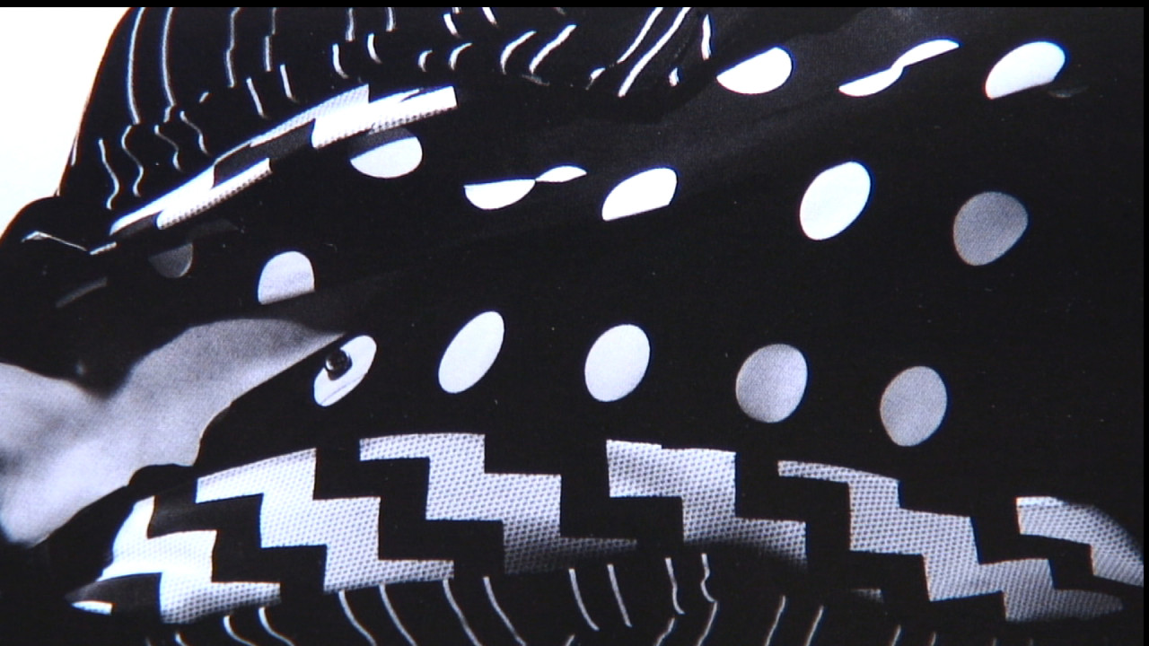 A close-up shot of black fabric patterned with white dots, stripes, and zigzags.