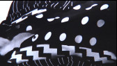 A close-up shot of black fabric patterned with white dots, stripes, and zigzags.