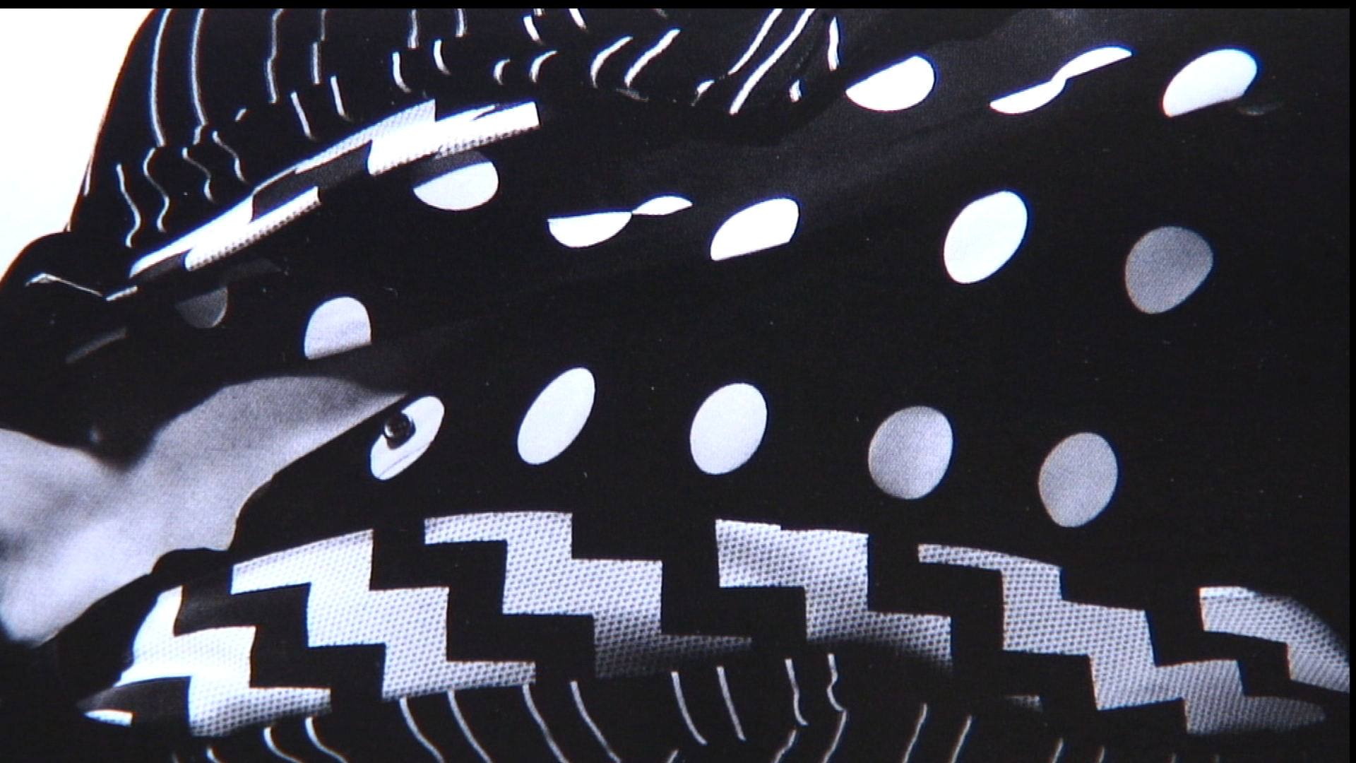 A close-up shot of black fabric patterned with white dots, stripes, and zigzags.
