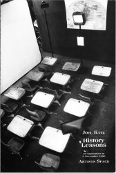 A black and white photograph, taken from above, of rows of school desks facing a television with a map behind it.