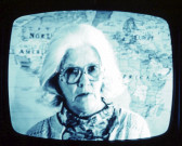 A close-up mage of a person wearing large glasses in front of a world map.
