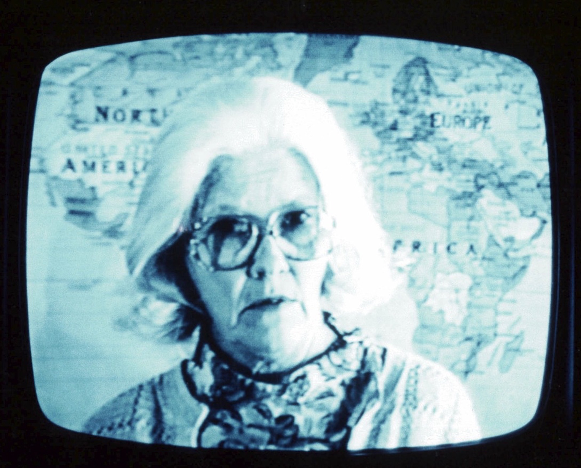A close-up mage of a person wearing large glasses in front of a world map.