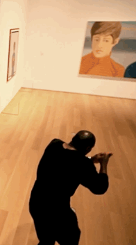 A moving image of a person, dressed in black, side stepping slowly in the gallery as the camera pans over to them.