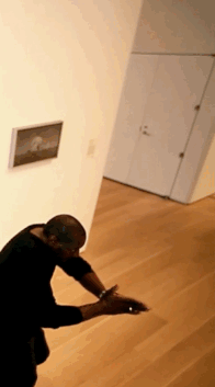 A gif depicting a person dressed in black with arms outstretched and clasped, moving slowly through a room.