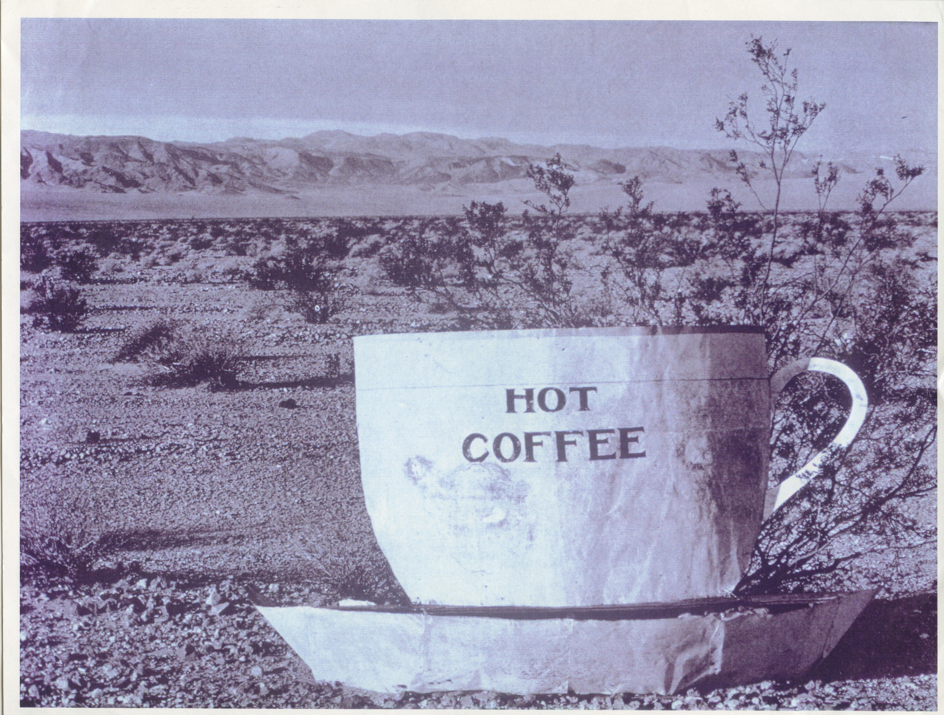 A slightly weathered sepia photograph of a sculpture of a white cup and saucer. Printed on the cup is the text 