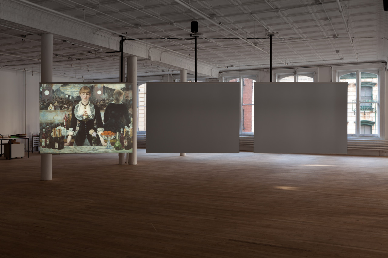 In a dimly lit room with light wood flooring and white pillars, three illuminated screens are suspended side-by-side from the ceiling. Two of the screens are off. The screen to the far left displays an image of a 19th century painting of a female bartender.