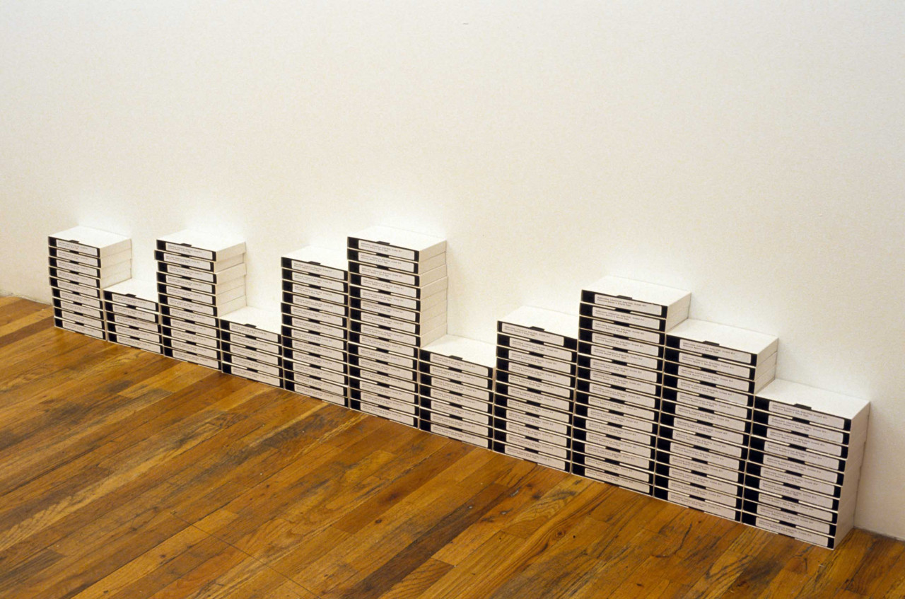 Stacks of labeled VHS tapes of varying heights arranged against a white wall.