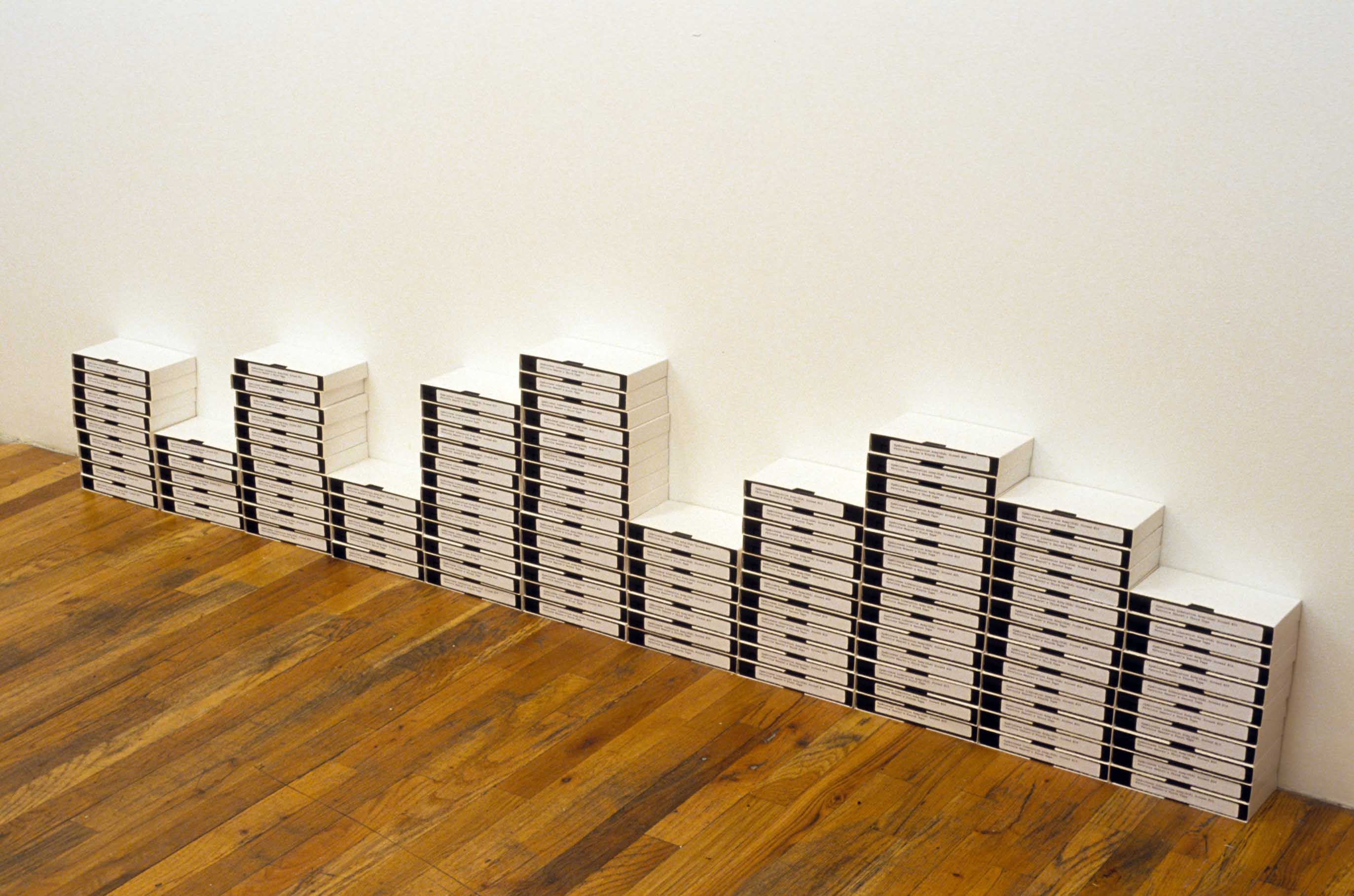 Stacks of labeled VHS tapes of varying heights arranged against a white wall.