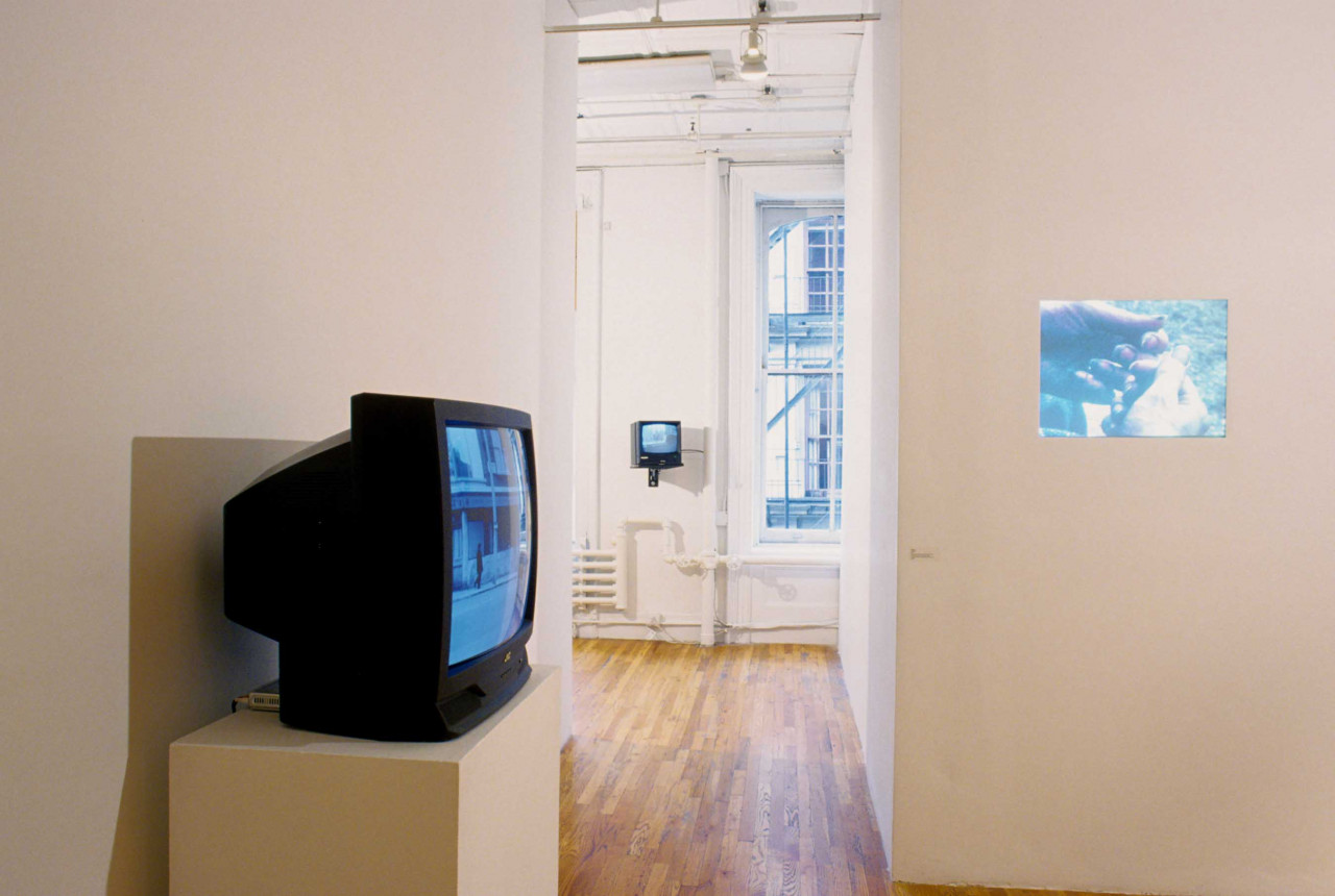 Two TV monitors installed in a gallery space with wooden flooring. One monitor is installed in the image