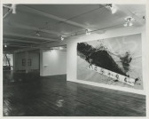 A black and white photograph of a gallery space. A piece with a large black paint swatch hangs on the wall on the right.