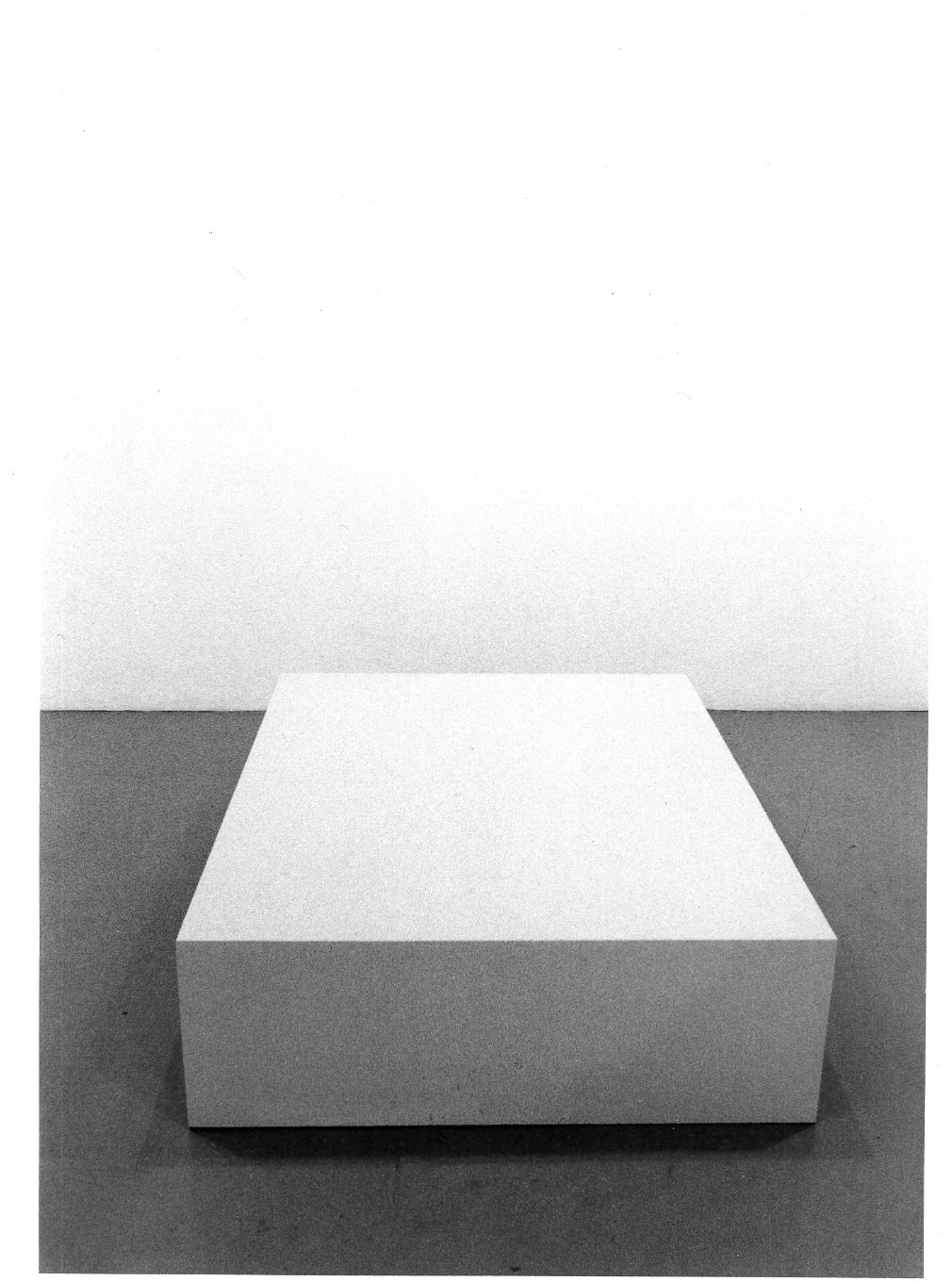 A black and white image of a sculpture resembling a rectangular prism displayed in the exhibition space.
