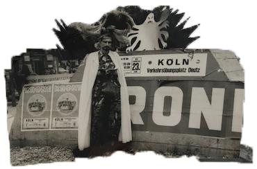 A black and white image with an organic border features Jack Smith in a white cloak standing in front of a wall. To the left of him are two posters that read, 