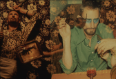 A double exposure divides a photograph into two scenes. On the left, a man reclines against a floral patterned ground next to a tray with a lobster. The man on the right holds a pair of sunglasses in his right hand while gazing towards a drink on the table in front of him.