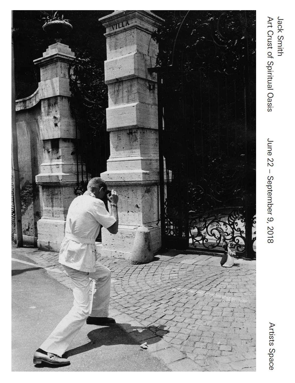A black and white image of a man photographing a plastic penguin in front of a decorative gate. Sideways text on the right reads, 