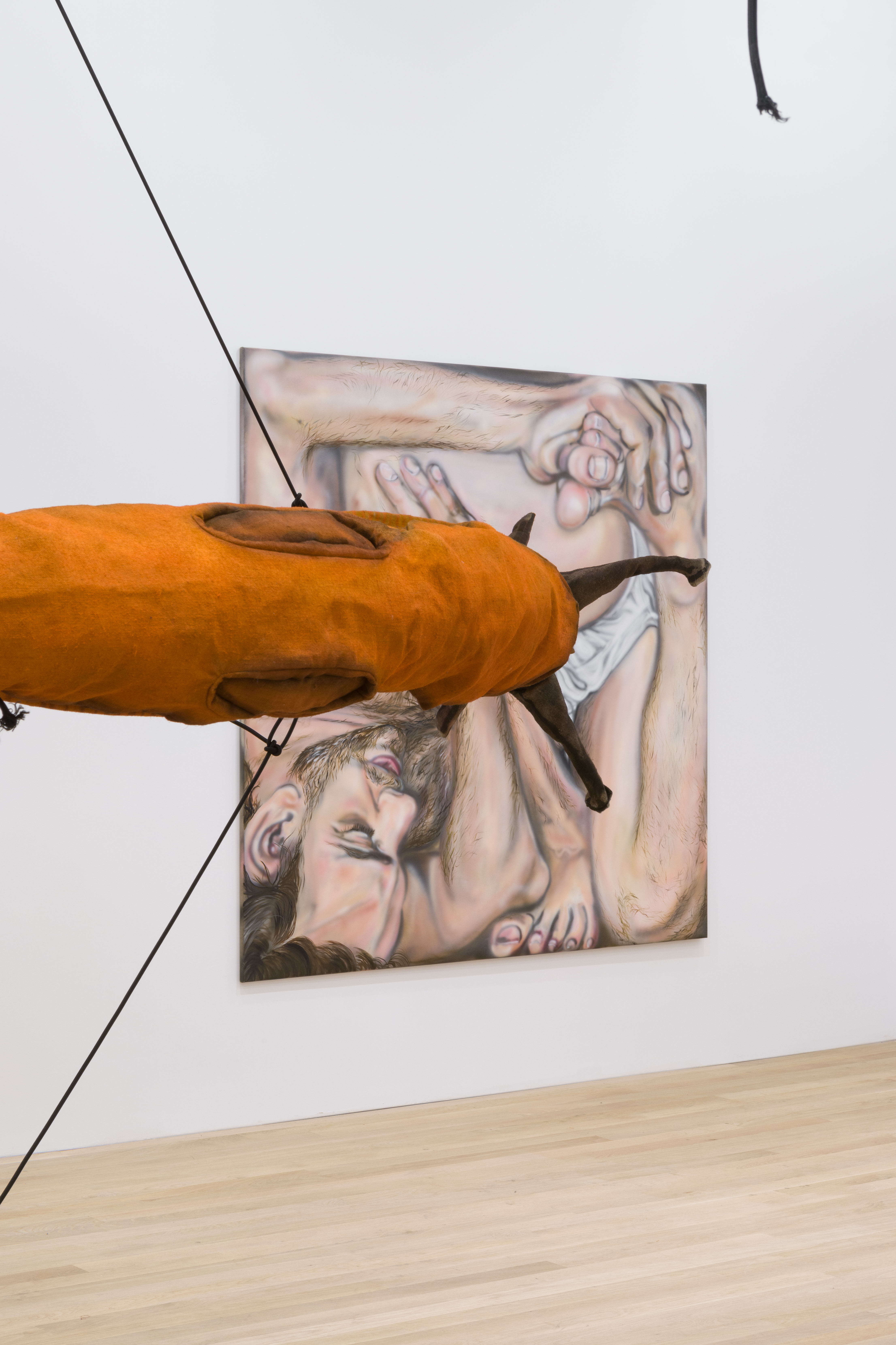A partial view of a large, orange circular slug sculpture is in front of a painting hanging in a white-walled gallery space.