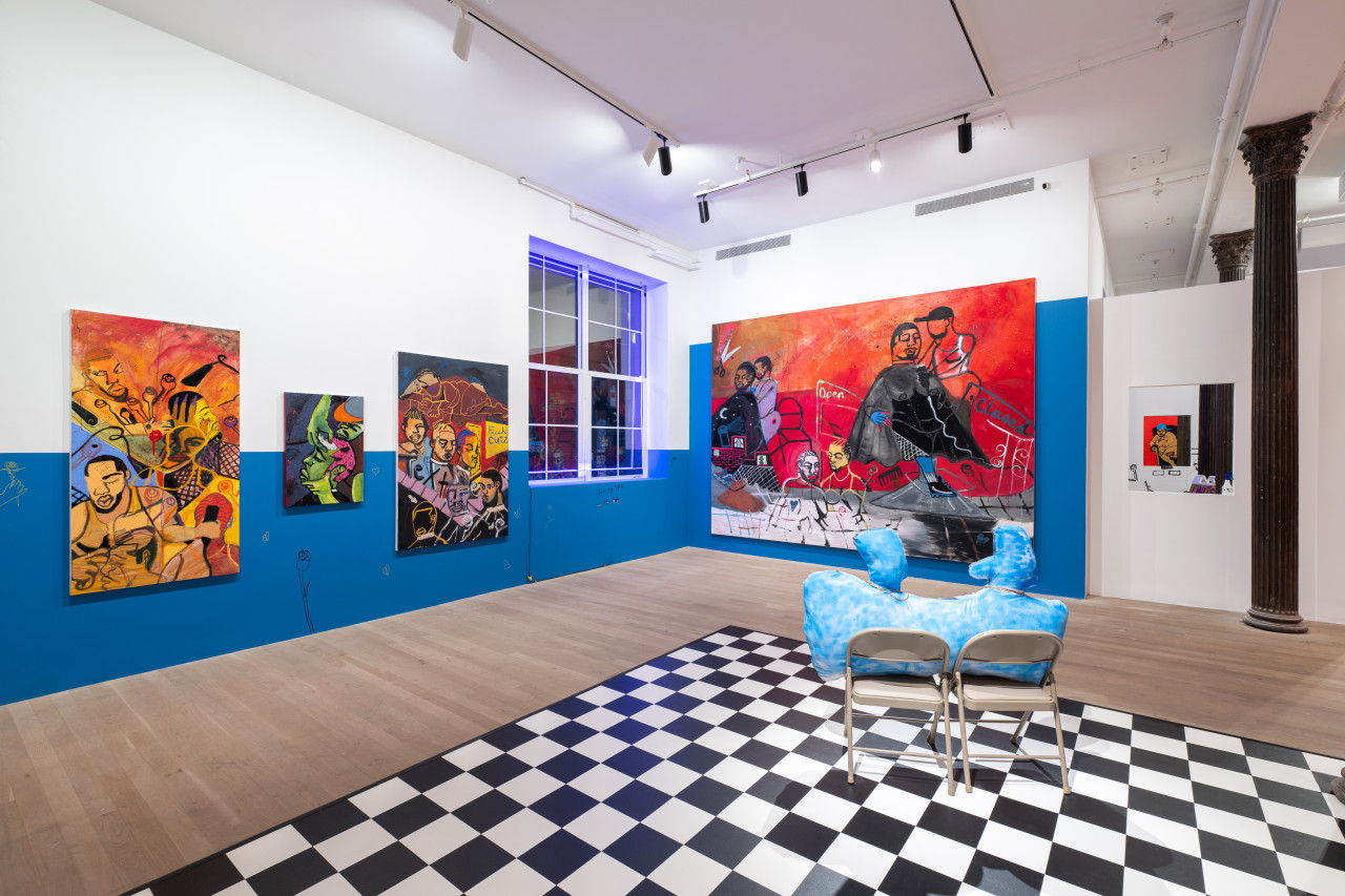 A color image of the corner of a gallery space. The walls are painted with blue accents, and there is a checkerboard floor. Large, vibrant paintings of Black Queer figures hang on the walls. Blue neon lights run along the frame of the window in the corner.