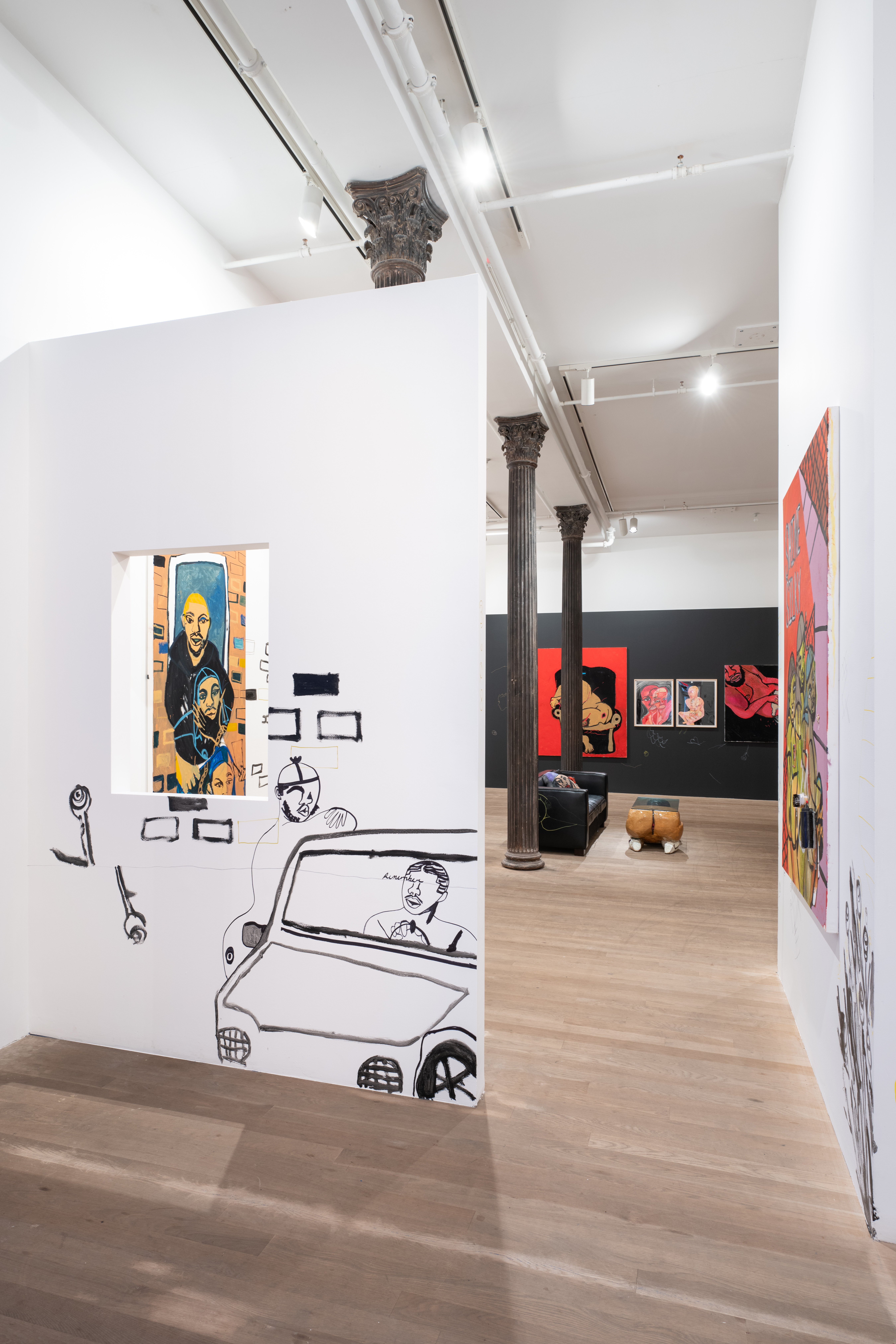 A color image of a gallery space. To the left of the image, on the foreground, a white wall with a window and a drawing of a parked car. The driver is speaking with a figure that leans on the car. Through the window, a painting of three figures is visible. In the background, four works hang on a black wall. In the center of the room, a black couch and a table in the shape of a body.