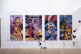 A color image of four large paintings hanging on a white wall. In the paintings, queer black bodies interact with each other in different settings, such as a hair supply store. Drawn directly on the wall, roses, a hand, a ring and other elements surround the paintings. At the center of the image, hair accesories sit on the floor.