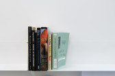 Six books on a white shelf against a white wall. From left, their authors are Saidiya Hartman, Augusto Boal, Fred Moten, Edward W. Said, Eric Williams, and James Baldwin.