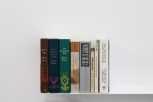 Eight books on a white shelf against a white wall. Five of the books are authored by Marcel Proust, two by William Shakespeare, and one by Samuel R. Delany.