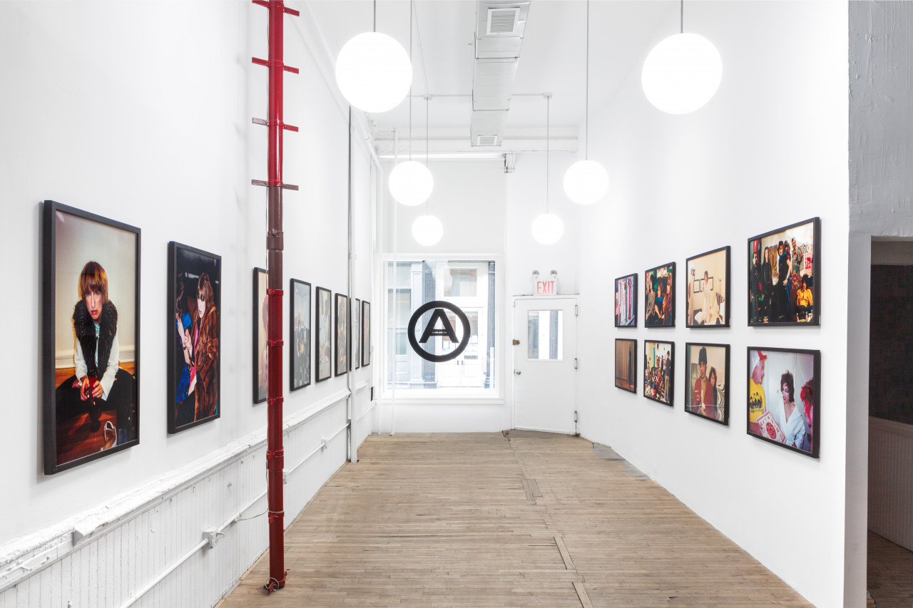 Film stills are framed and lines up against two sides of a room, leading to a window with the black Artists Space logo.