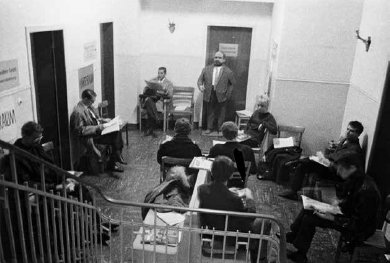 A room, view from above a stair case, with a group of men sat scatted around the area.