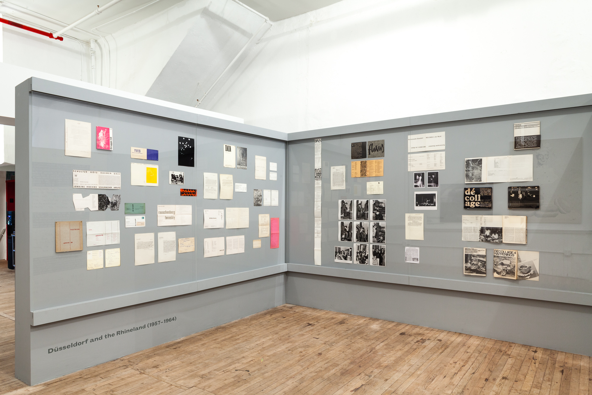 An angled view of two adjacent gray walls displaying various paper material, documents, and photographs.