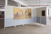 Two unframed paintings are hung on a foldable room divider in a gallery. The larger painting depicts the interior of a classroom with four ambiguous figures. The smaller painting shows a man poised mid-dance.