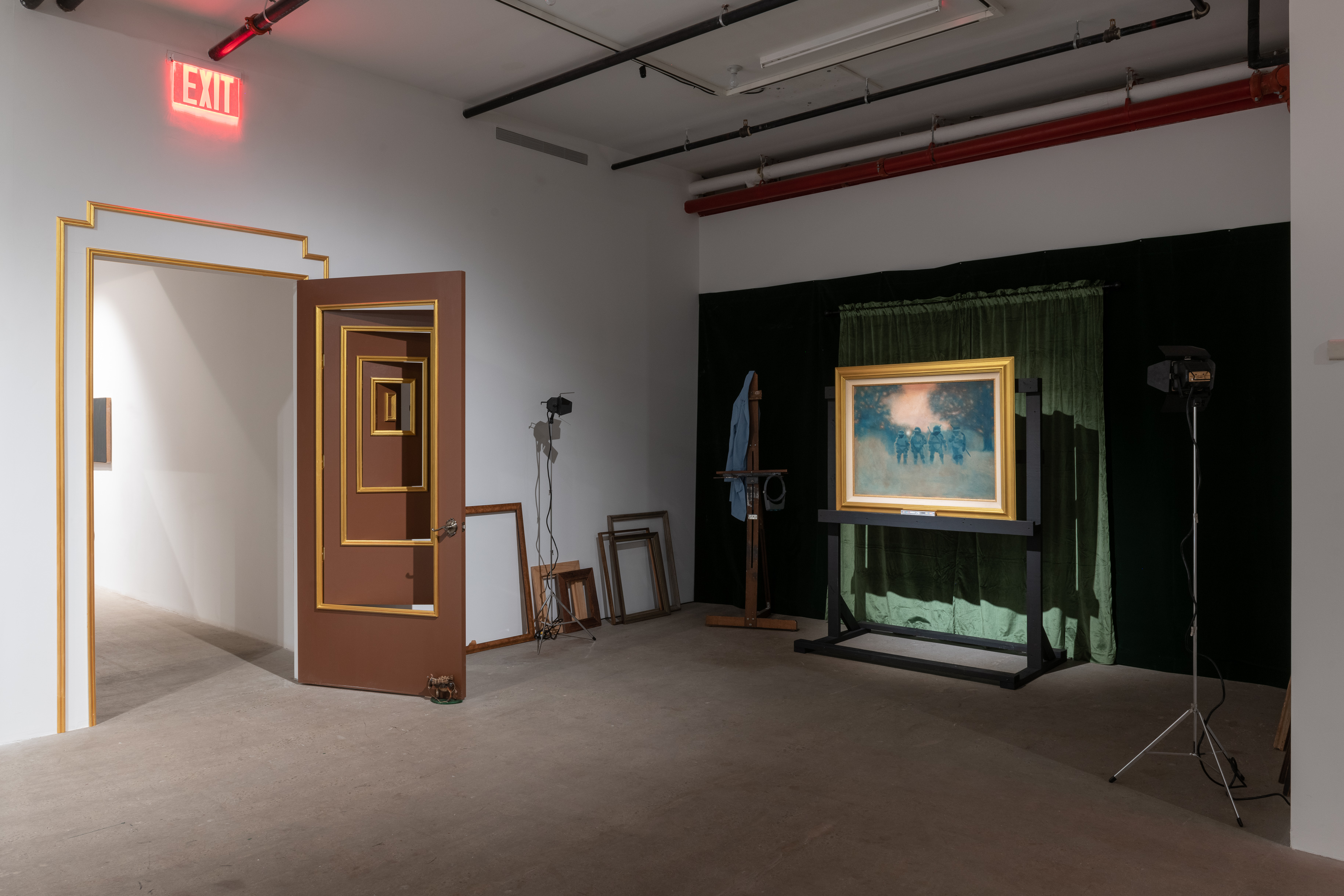 A color photograph of a door with multiple nested smaller doors within the doorframe. Each individual doorway is framed with a gold outline. To the left are several empty picture frames and two studio lights. In front of dark green curtains is a painting set in a gold frame.