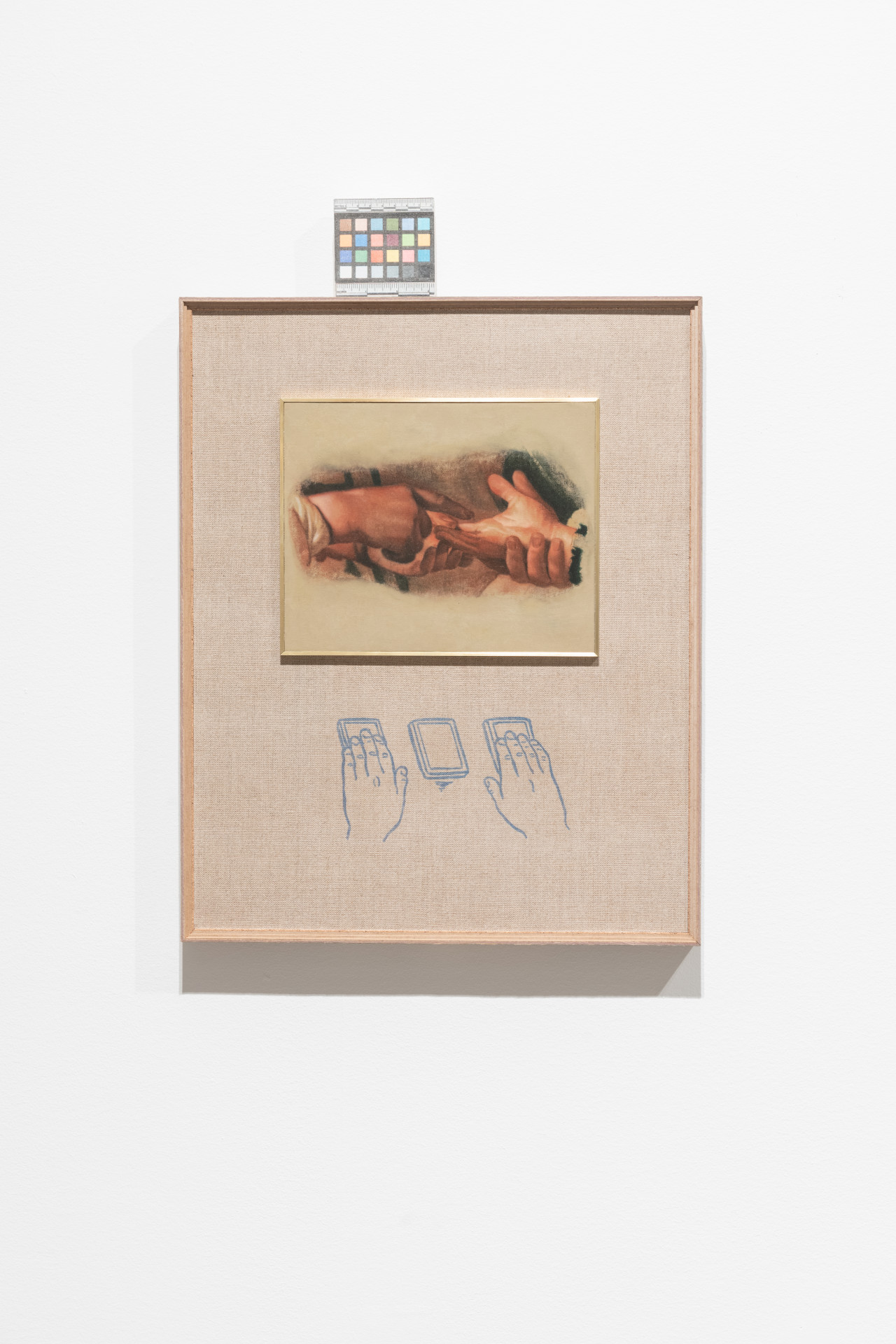 A color photograph of a framed painting of two sets of hands. On top of the frame rests a color control strip.